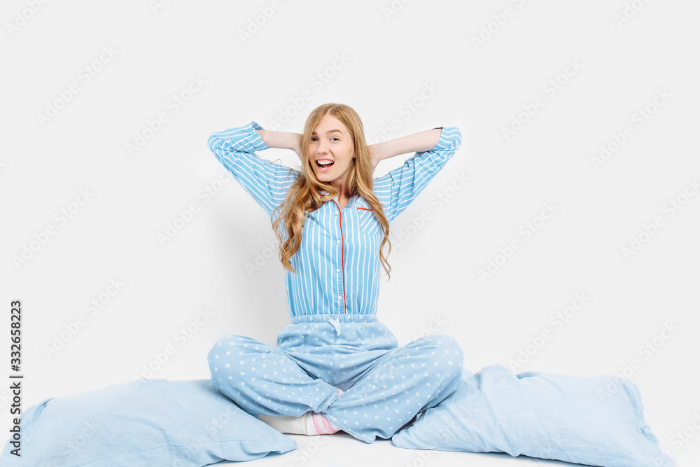 Beautiful girl in pajamas, sitting on the bed with pillows in her hands, on a white background Beautiful girl in pajamas, sitting on the bed with pillows in her hands, on a white background
