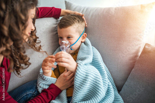 Fotografie Mother helps her little boy to makes inhalation at home