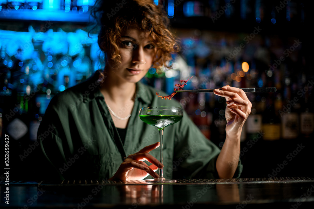 young woman at bar holds glass with cocktail and decorates it