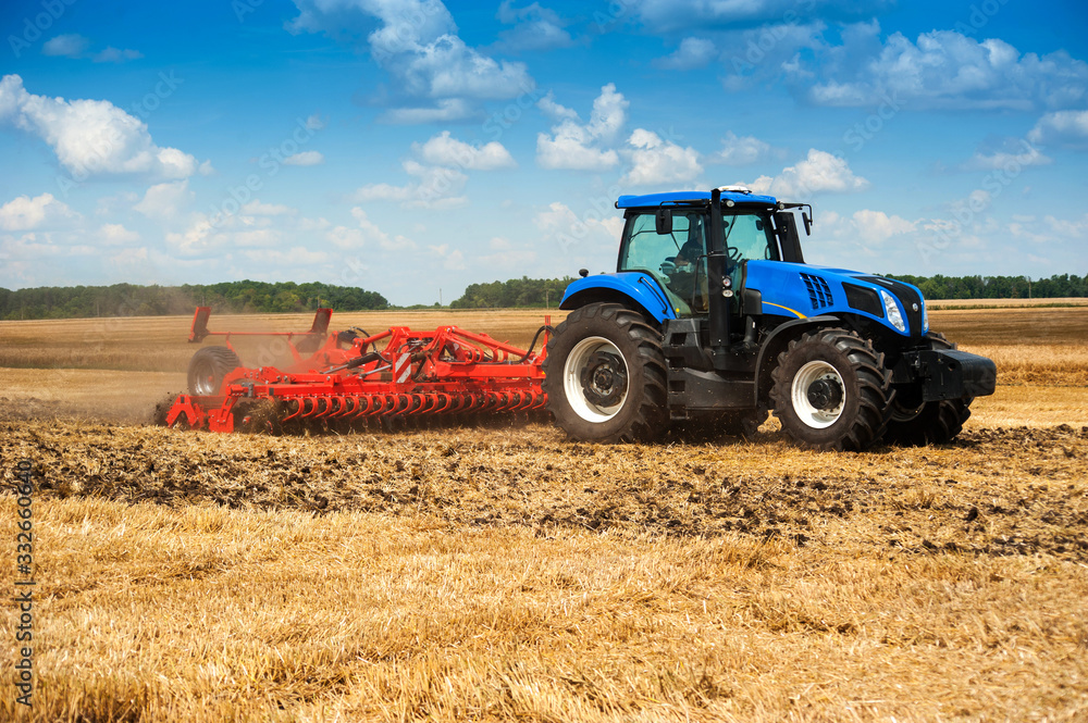 Naklejka premium niebieski nowy ciągnik ciągnie czerwoną bronę, podnosi pył na polu, przygotowuje glebę