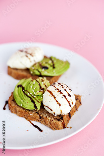 Breakfast toast with poached egg and avocado on the white plate. Pink background