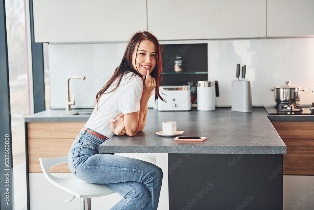 Young beautiful brunette in casual clothes sits in kitchen with fresh drink at morning time Young beautiful brunette in casual clothes sits in kitchen with fresh drink at morning time