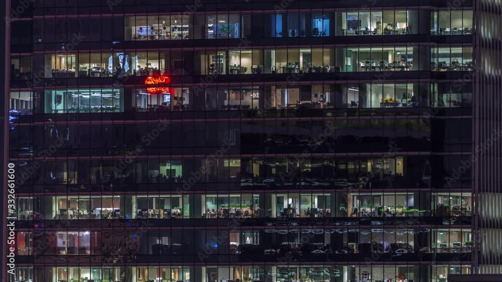 Modern office building with big windows at night timelapse close up view, in windows glowing light shines and some people inside, Singapore. Pan up Modern office building with big windows at night timelapse close up view, in windows glowing light shines and some people inside, Singapore. Pan up