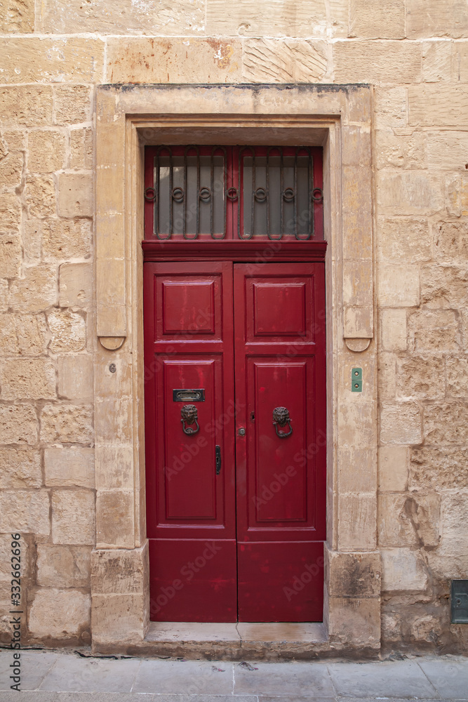 Vintage red wooden door in yellow stone wall. Malta