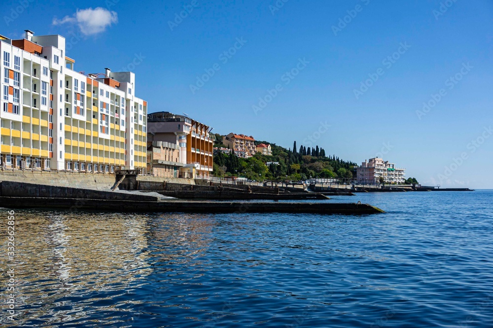 Yalta, Russia - September 30, 2019: View of coastline with breakwaters and hotels along shore against background of Crimean mountains. Selective focus. Clear sea is dark blue.