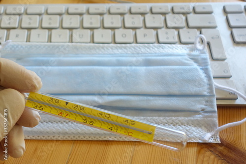 Virus season, pandemic. Smart working in order to prevent the spread of respiratory diseases like coronavirus COVID-19. Latex glove, surgical mask, mercury thermometer on a computer keyboard