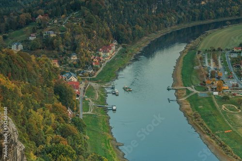 Viewpoint from the Bastei bridge in the evening. River Elbe with a view of the spa town of Rathen. Rocks and trees in autumn. Buildings, ship and ferry on the river