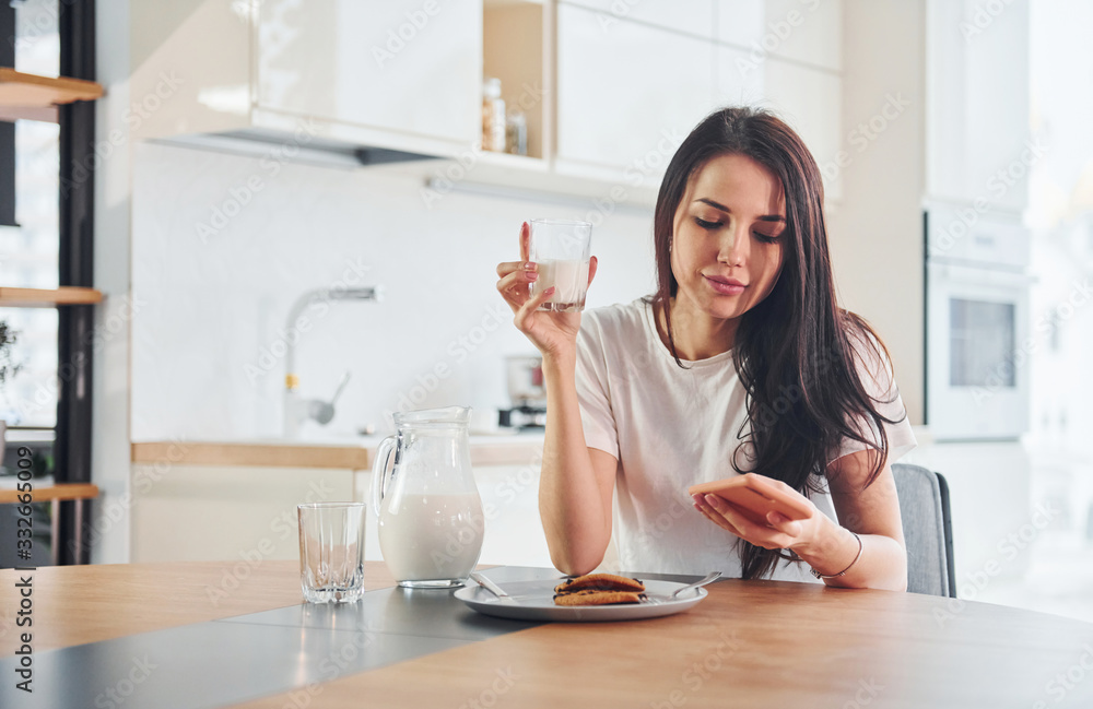 Young beautiful brunette in casual clothes with sweets and glass of milk in kitchen at daytime Young beautiful brunette in casual clothes with sweets and glass of milk in kitchen at daytime