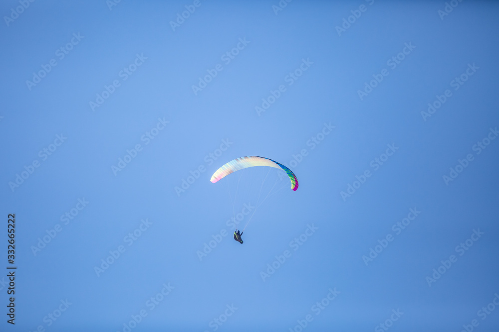 Skydiver with a colorful canopy of a parachute on the background a blue sky Skydiver with a colorful canopy of a parachute on the background a blue sky