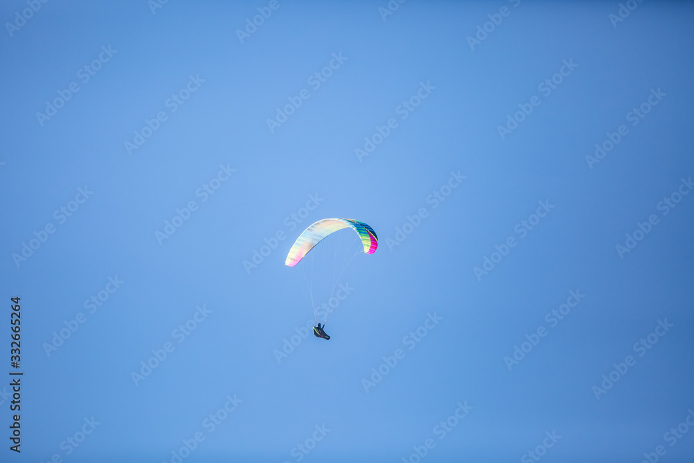 Skydiver with a colorful canopy of a parachute on the background a blue sky