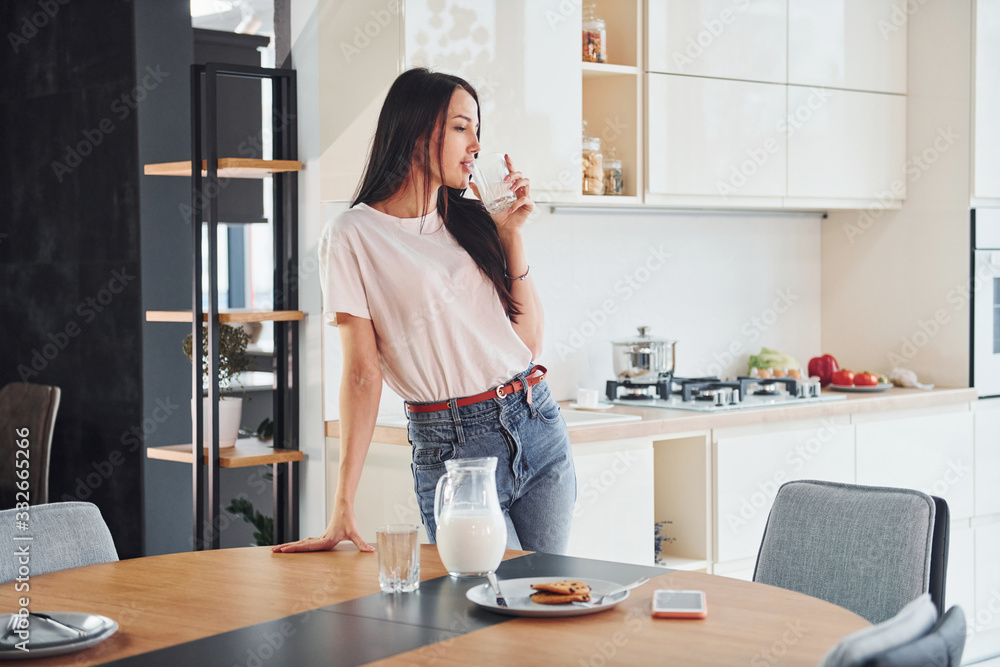 Young beautiful brunette in casual clothes indoors in kitchen at daytime near table with milk and cookies Young beautiful brunette in casual clothes indoors in kitchen at daytime near table with milk and cookies