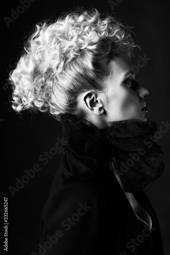 A beautiful blonde girl with an elegant hairstyle and large breasts, wearing a bra, scarf and a blazer, poses in the dark. Trendy, commercial and advertising design. Close Up monochrome portrait.