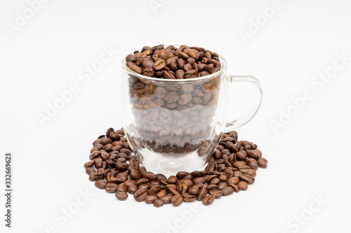 Glass thermos insulating cup transparent overfilled with roasted coffee beans on white underground