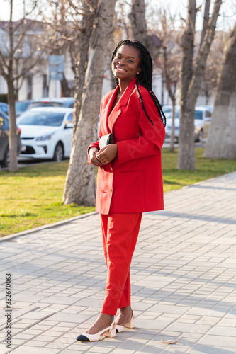 Close up portrait of a beautiful young african american woman with pigtails in a red business suit smiling and walking along the street © Nana_studio