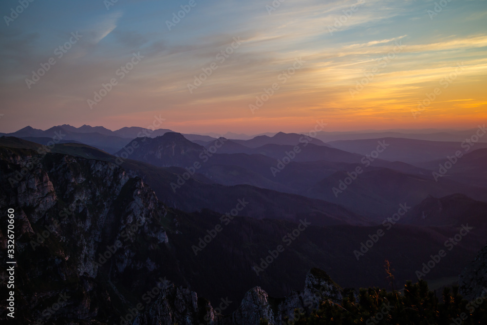 Purple silhouettes of Carpathian rocky mountains and sunset orange-blue sky with clouds Purple silhouettes of Carpathian rocky mountains and sunset orange-blue sky with clouds