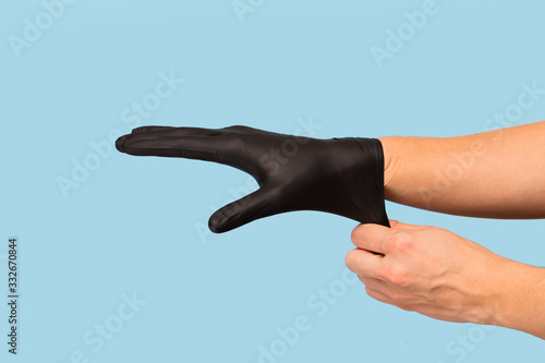 man puts on sterile black gloves on a blue background. Hazard, hygiene, control