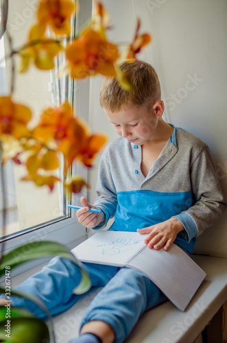  A child in blue pajamas is sitting by the open window. On the windowsill is a pot with a blooming flower.