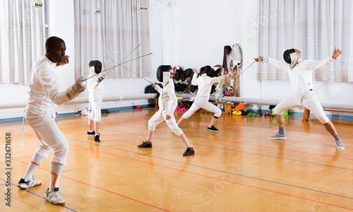 Coaches demonstrating to young athletes attack movements with rapier during fencing workout