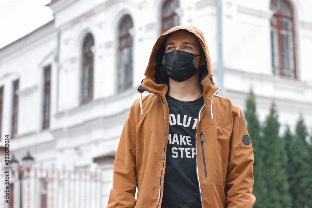 Stylish young man in black face mask on the city street. Coronavirus quarantine situation. Street style during the epidemic. Protection medical respirator as pandemic clothing item. Pandemic lifestyle Stylish young man in black face mask on the city street. Coronavirus quarantine situation. Street style during the epidemic. Protection medical respirator as pandemic clothing item. Pandemic lifestyle