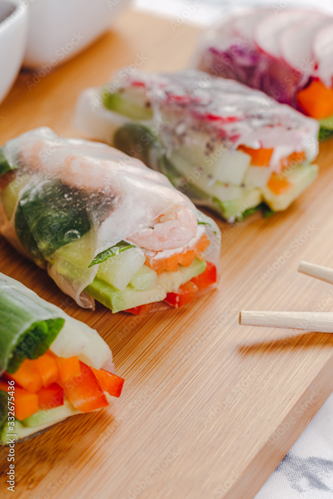 Delicious asian dish. Side view of fresh spring rolls with shrimp and vegetables and different sauces served on a wood plate with chop sticks. Delicious asian dish. Side view of fresh spring rolls with shrimp and vegetables and different sauces served on a wood plate with chop sticks.