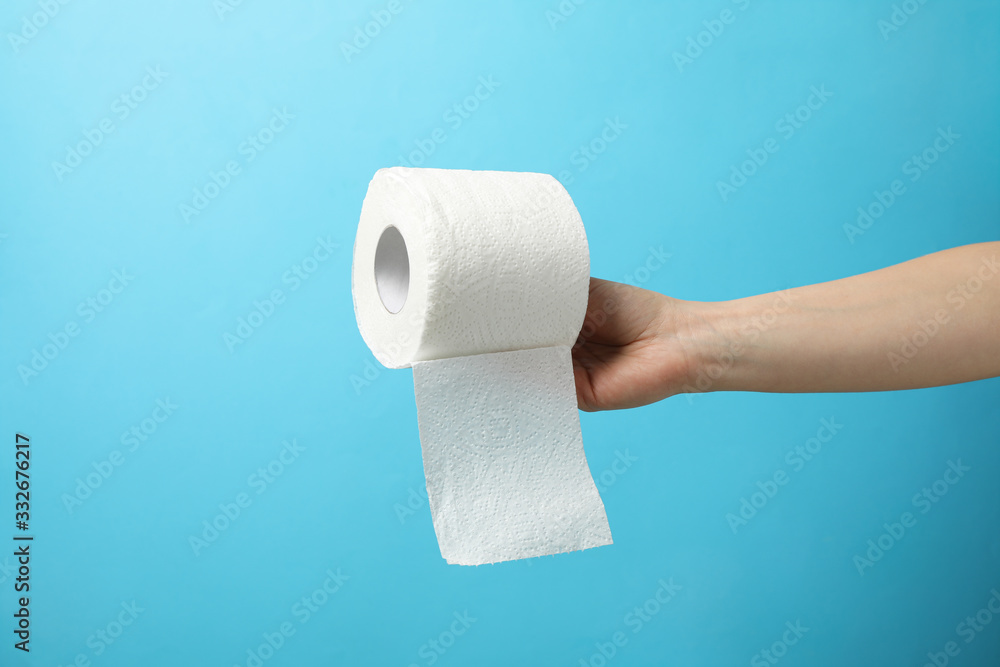 Obraz premium Hand holds roll of toilet paper on blue background