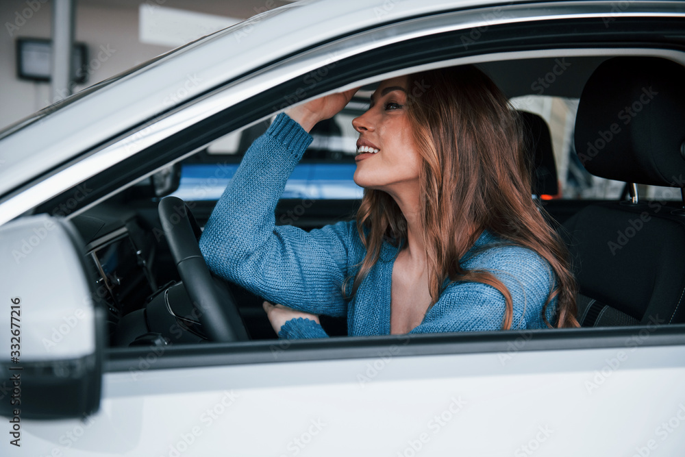 Positive woman in blue shirt sits inside of new brand new car. In auto salon or airport Positive woman in blue shirt sits inside of new brand new car. In auto salon or airport