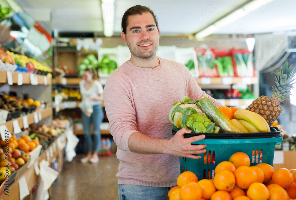 Man standing with full grocery cart during shopping in fruit shop