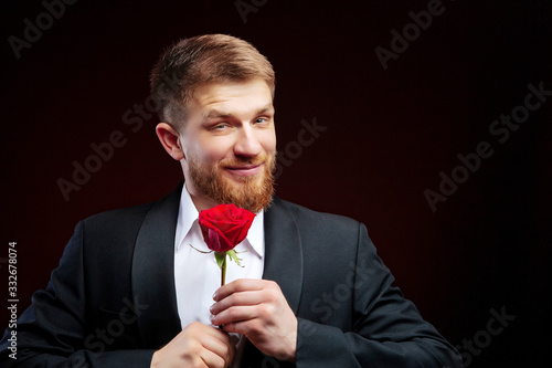 Close up of handsome boyfriend holding red rose. Bearded man is ready for 8th of March.