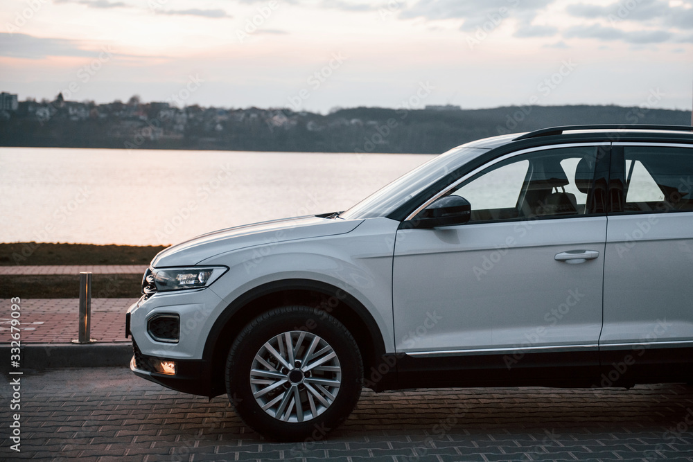 Particle side view of modern white car parked near lake at evening time