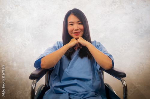isolated portrait of young beautiful and happy Asian Korean woman in hospital patient gown sitting on wheelchair smiling positive recovering from accident or virus infection