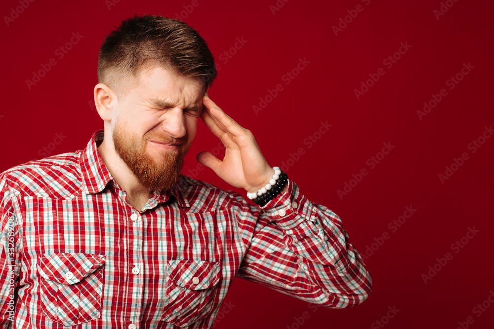 Tired young bearded man checked shirt has a headache. Redhead man holding hands on head, suffering. Tired young bearded man checked shirt has a headache. Redhead man holding hands on head, suffering.