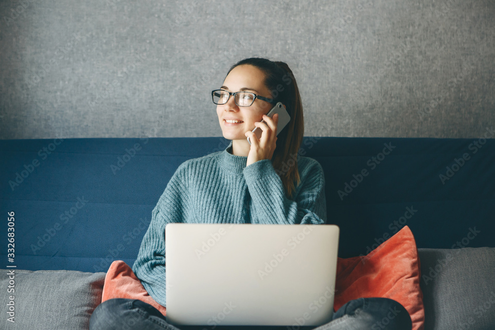 A girl works from home or a student is studying from home or a freelancer. She uses a laptop and a phone.