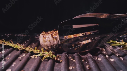 Delicious juicy meat steak cooking on grill. Kitchen tongs. Aged prime rare roast grilling tenderloin fresh marble tenderness beef. Prime beef fry on electric roaster, rosemary black pepper, salt. photo