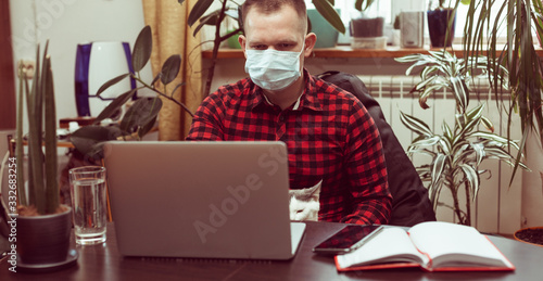 Work at home in quarantine conditions. A masked man sits at a laptop