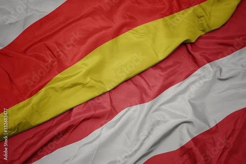 waving colorful flag of austria and national flag of south ossetia.