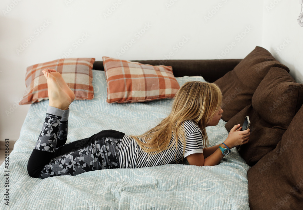 Obraz premium Covid-19. Home school concept. 9 year old girl is bored at home with a mobile phone.