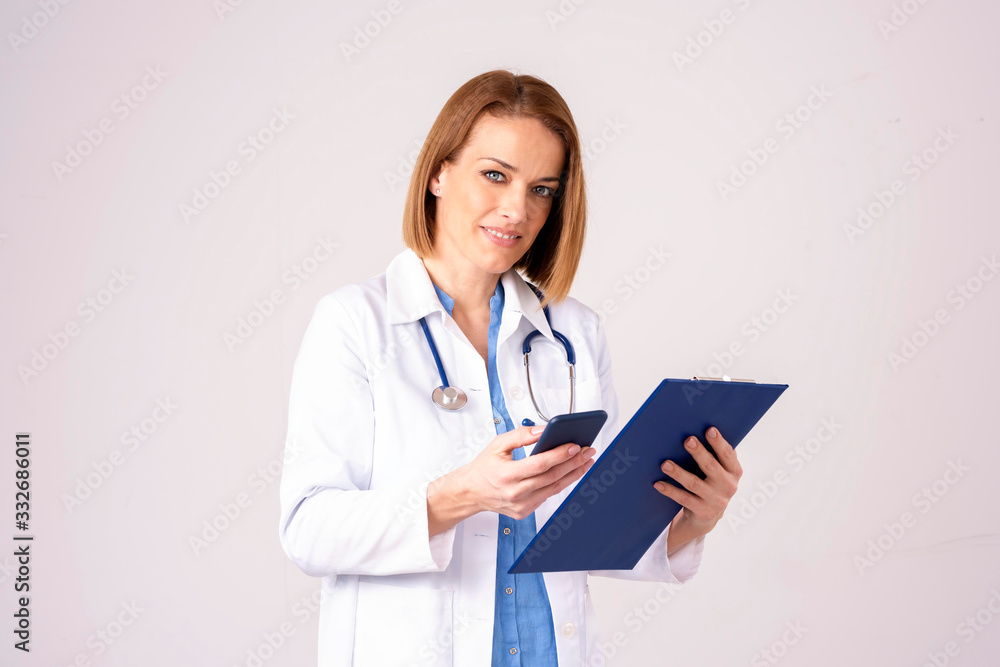 Middle aged female doctor text messaging while standing at isolated background Middle aged female doctor text messaging while standing at isolated background