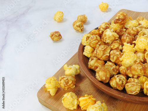 High angle view of delicious popcorn in round wooden plate isolated on gray marble background. Include buttery caramel corn and rich cheddar cheese corn. Food and snack concept. With copy space.
