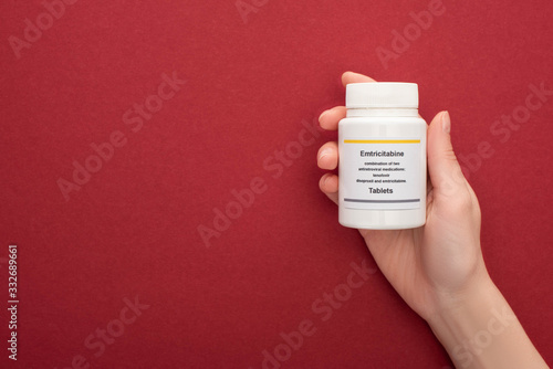 cropped view woman holding of container with emtricitabine tablets on red background photo