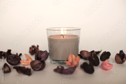 A candle in a glass with flowers scattered around. Burning candle in a glass on a white background. Flowers on a white background with a candle. photo