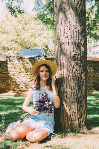 A young girl is resting and walking in the Park in a blue dress with a hat and flowers