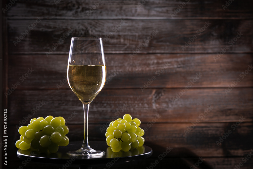 Fototapeta premium White wine glass with grapes on a table on a wooden background