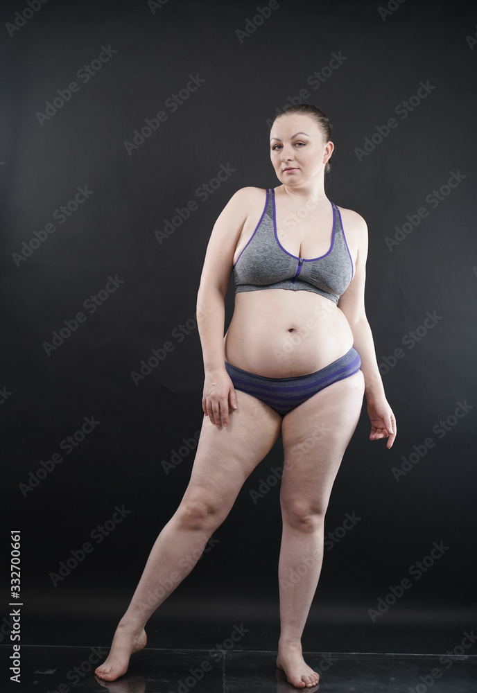 Obraz premium plus size woman shows her body in stretch marks and hair with cellulite and encourages you to love and accept yourself in any way . black background in the Studio. full- length photo.