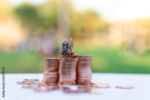 Miniature people: Old couple figure sitting on stack of coins . Image use for background retirement planning, Life insurance concept.