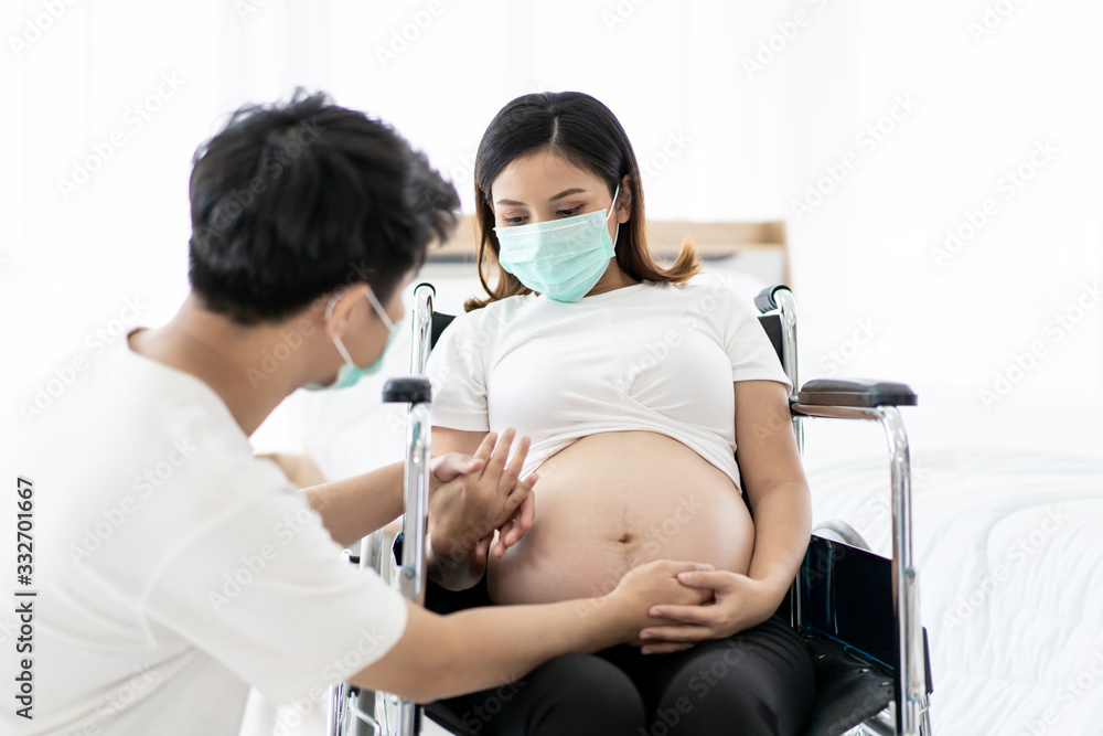 Husband take care his pregnant wife sitting on a wheelchair, husband stay beside his wife. Pregnant woman and husband protect themself from COVID19 disease, COVID-19 and 2019-nCov world crisis issue. Husband take care his pregnant wife sitting on a wheelchair, husband stay beside his wife. Pregnant woman and husband protect themself from COVID19 disease, COVID-19 and 2019-nCov world crisis issue.