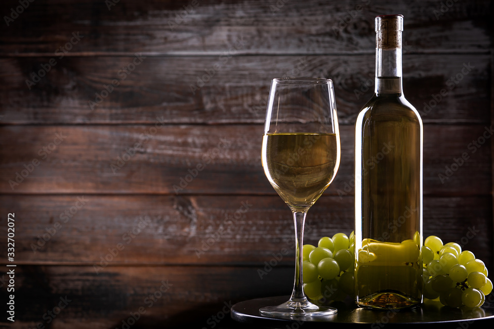 White full wine bottle and wineglass with grapes on a table on a wooden background