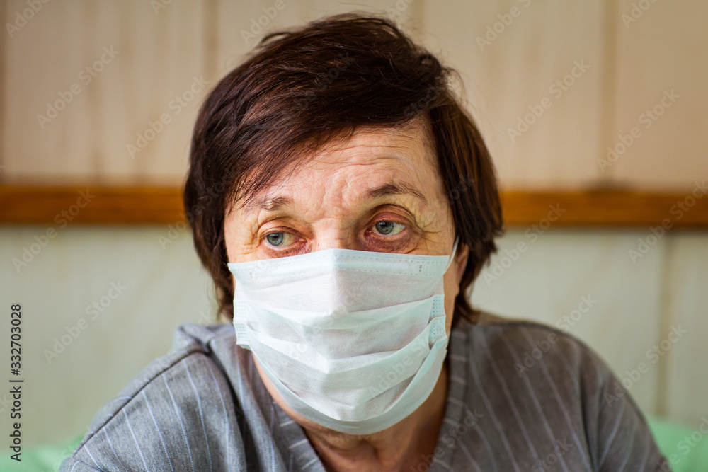 an adult woman, a pensioner, with a bottle of dizenfektor , and a medical mask, is in home quarantine, because of COVID-19 an adult woman, a pensioner, with a bottle of dizenfektor , and a medical mask, is in home quarantine, because of COVID-19