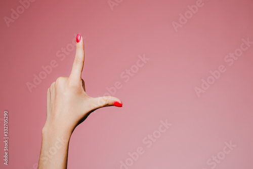 Woman's hands with bright manicure isolated on pink background L letter photo