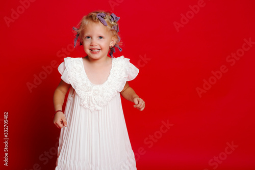 Happy young blonde curly model girl smiling showing white dress isolated on red