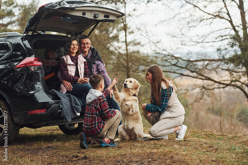 Happy family have fun with their dog near modern car outdoors in forest